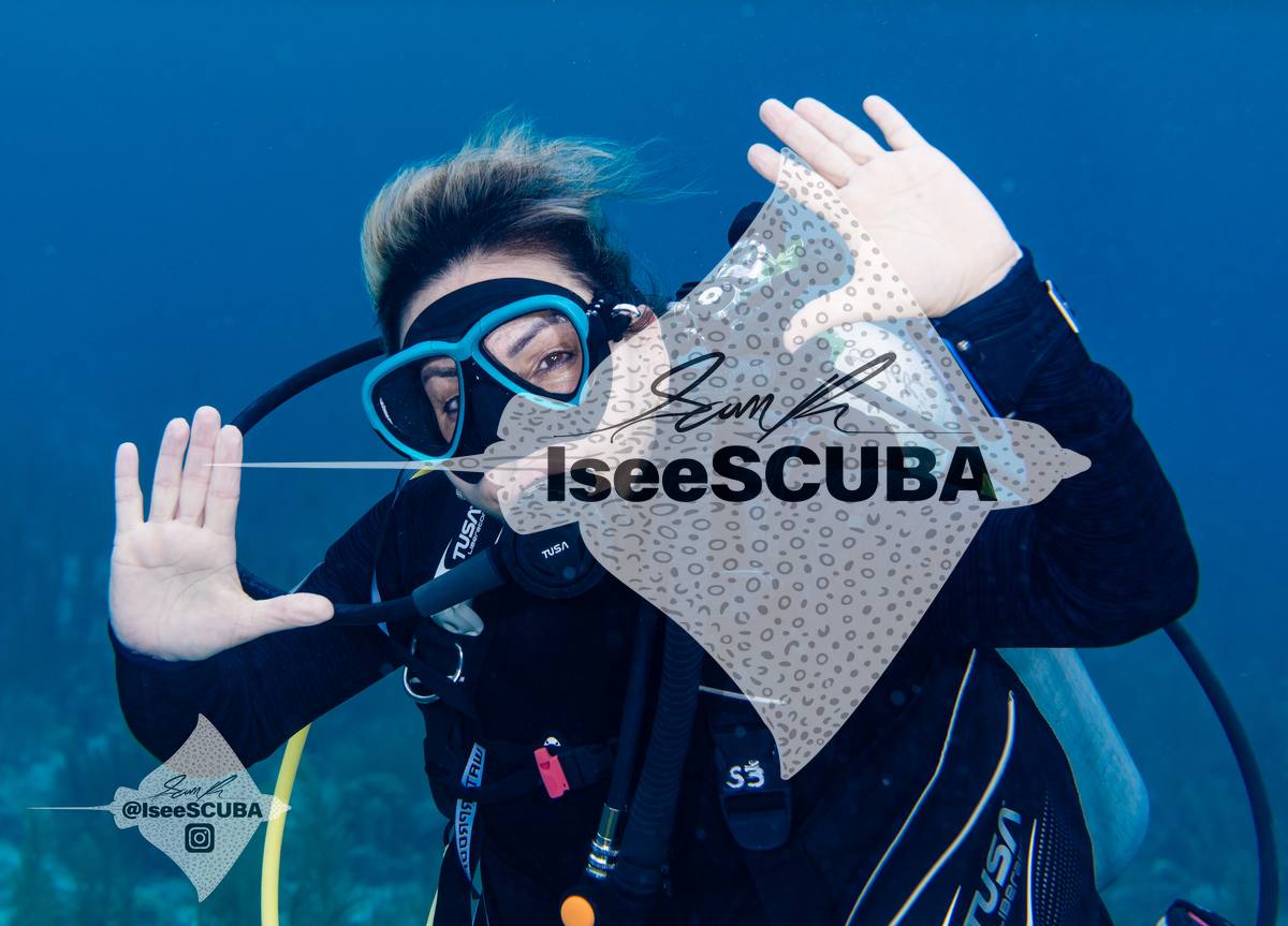 Diver with a blue mask raising both hands toward the camera.