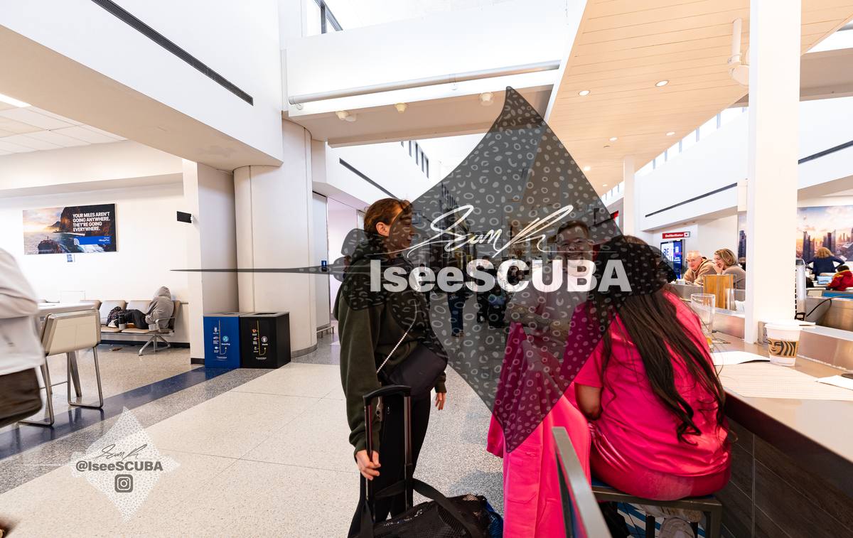Travelers gathered at a counter in a bright airport terminal.
